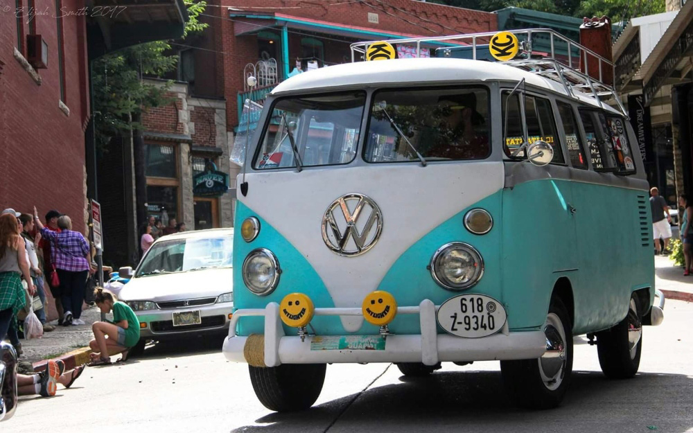 Classic turquoise VW Bus cruising through a festival crowd, full of retro charm and character.
