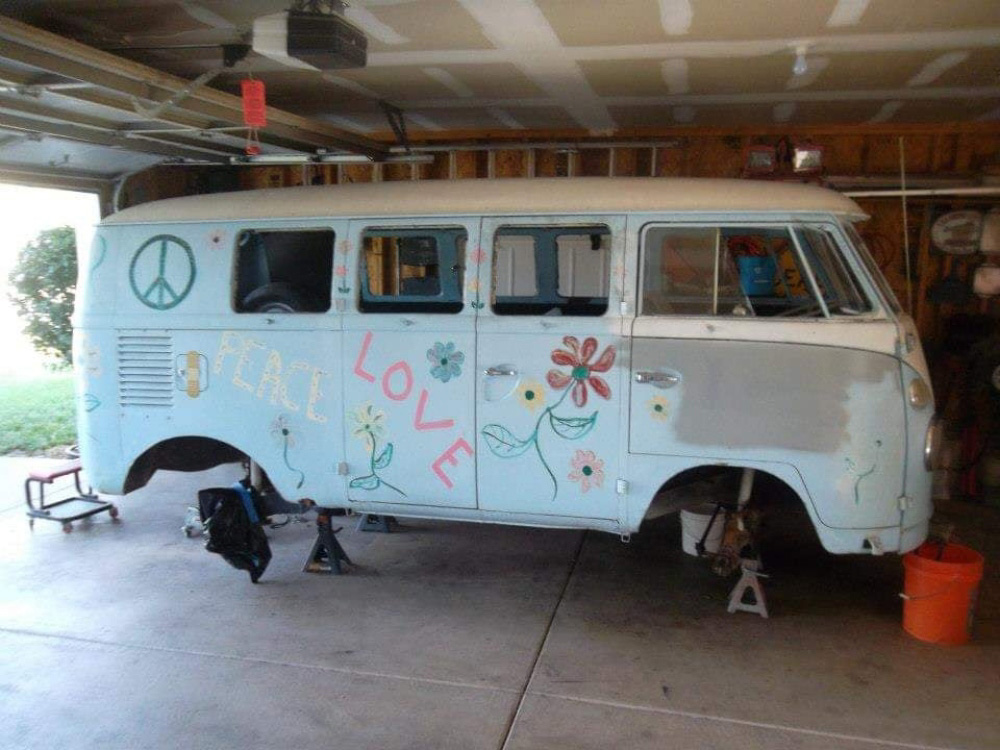 Vintage VW Bus in a garage before restoration, elevated on stands with wheels removed.
