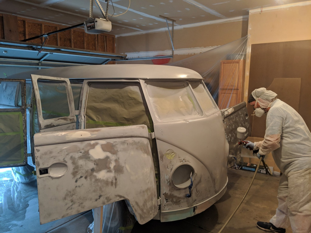 VW Bus being spray-painted inside a garage during the restoration process.