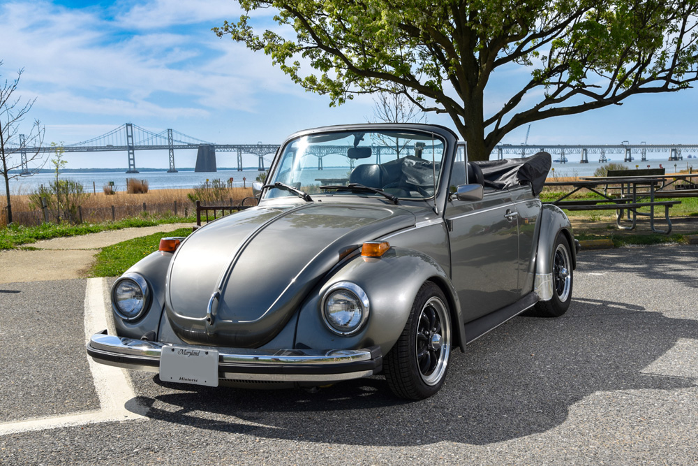 1979 Volkswagen 1303 Super Beetle convertible parked by the water with a bridge in the background