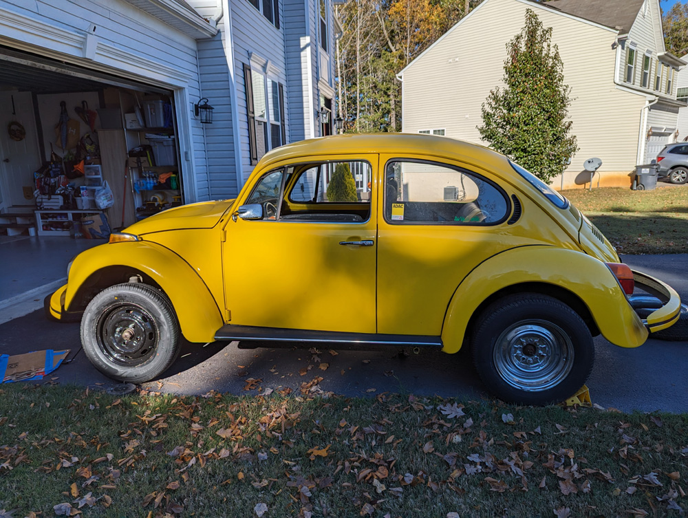 Yellow Volkswagen Beetle parked in a residential driveway with a garage in the background