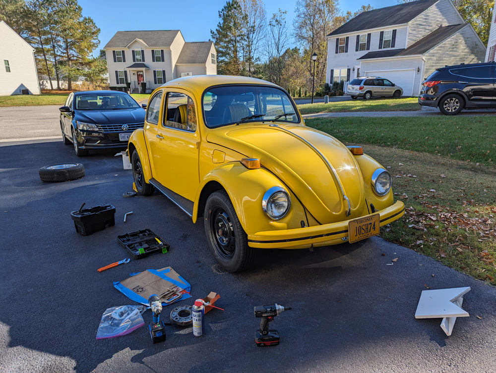 Yellow Volkswagen Beetle on a driveway surrounded by tools and parts during maintenance work