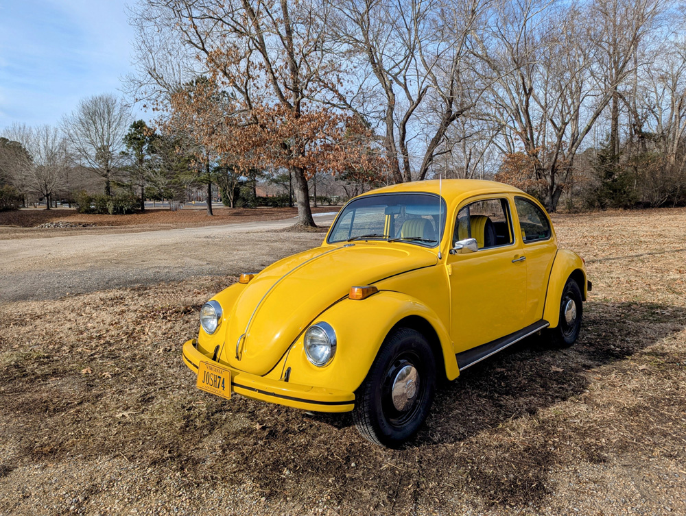 Yellow Volkswagen Beetle with JOSH74 license plate parked on grass with trees in the background