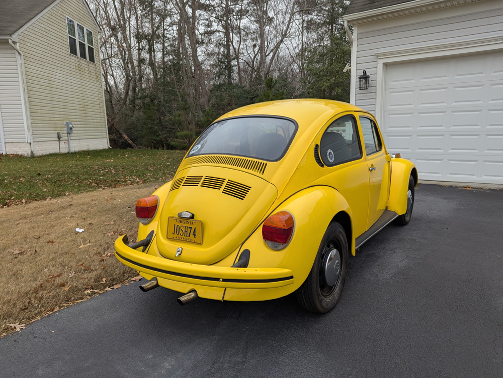 Yellow Volkswagen Beetle with JOSH74 license plate parked in a driveway in front of a garage