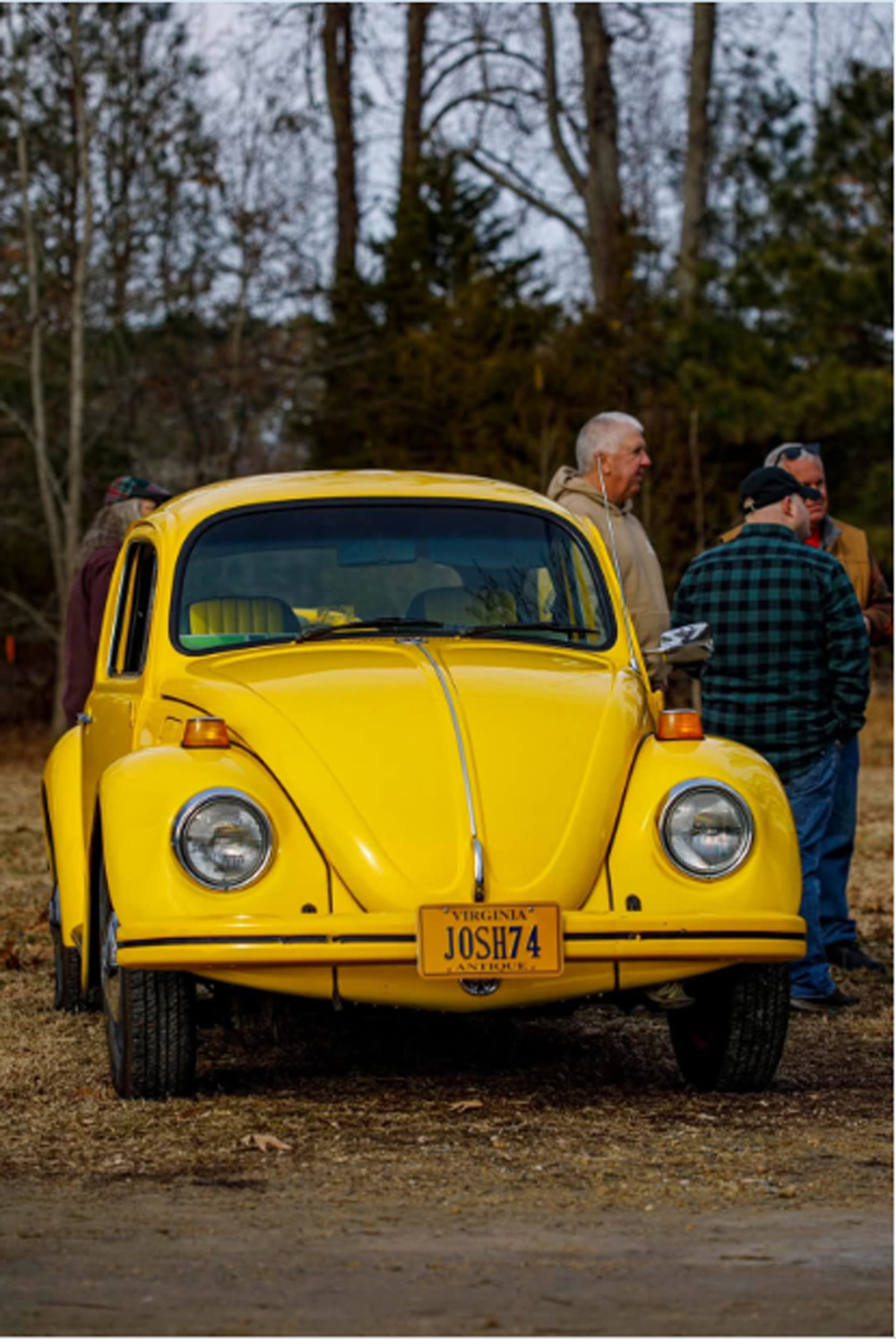 Yellow Volkswagen Beetle with JOSH74 license plate parked outdoors with people gathered nearby