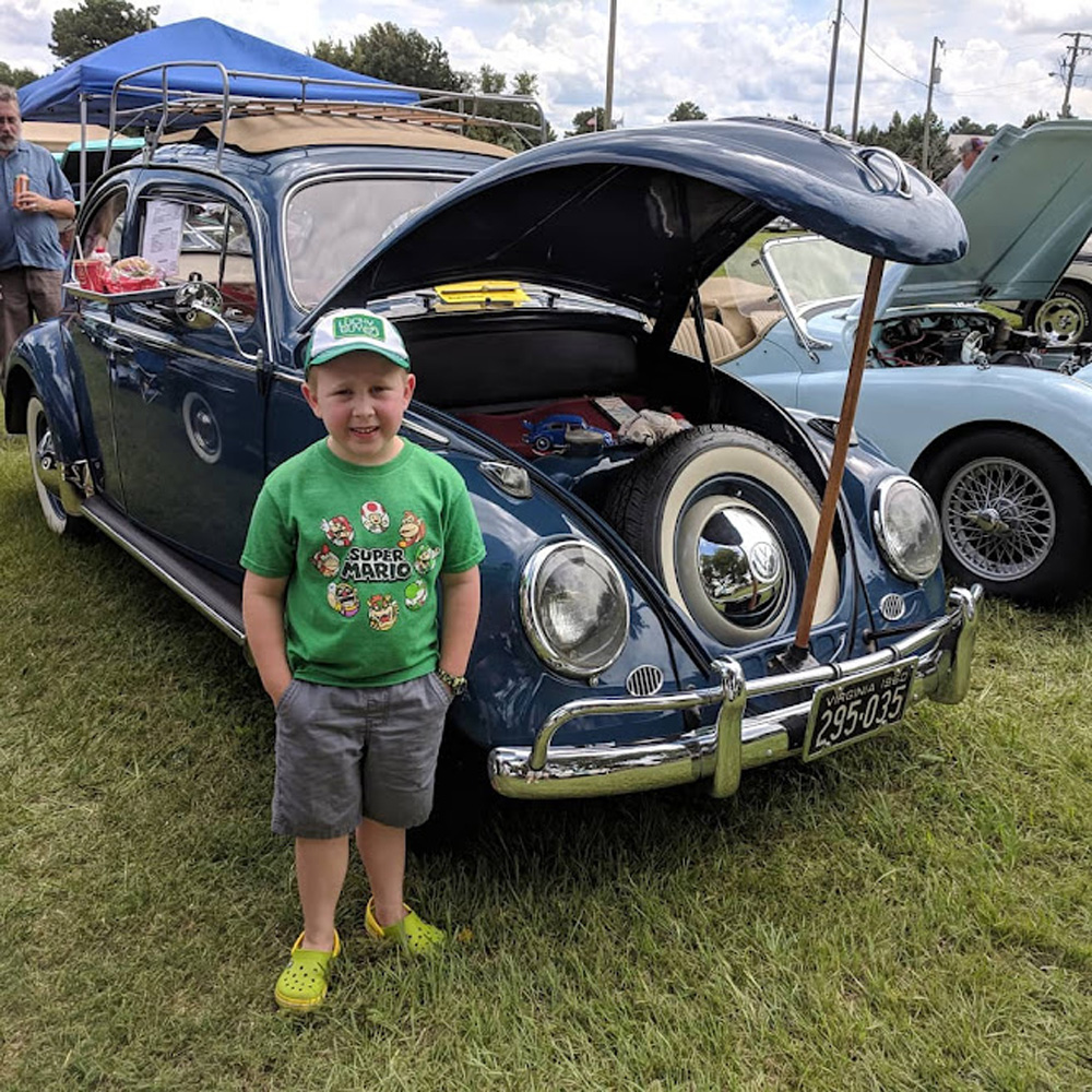 Josh standing in front of a dark blue Volkswagen Beetle with the front trunk open at a car show