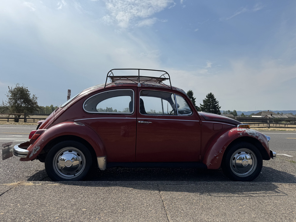 Red Volkswagen Beetle parked on a rural roadside with roof rack and worn paint