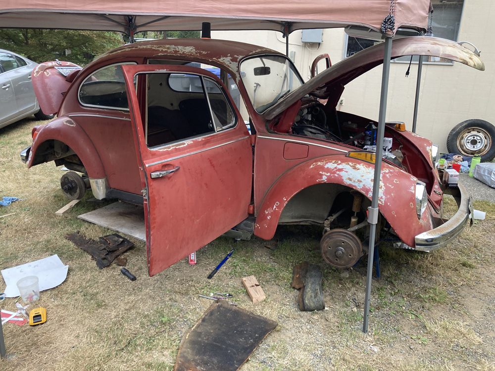 Red Beetle under a canopy with hood open and wheels removed during restoration