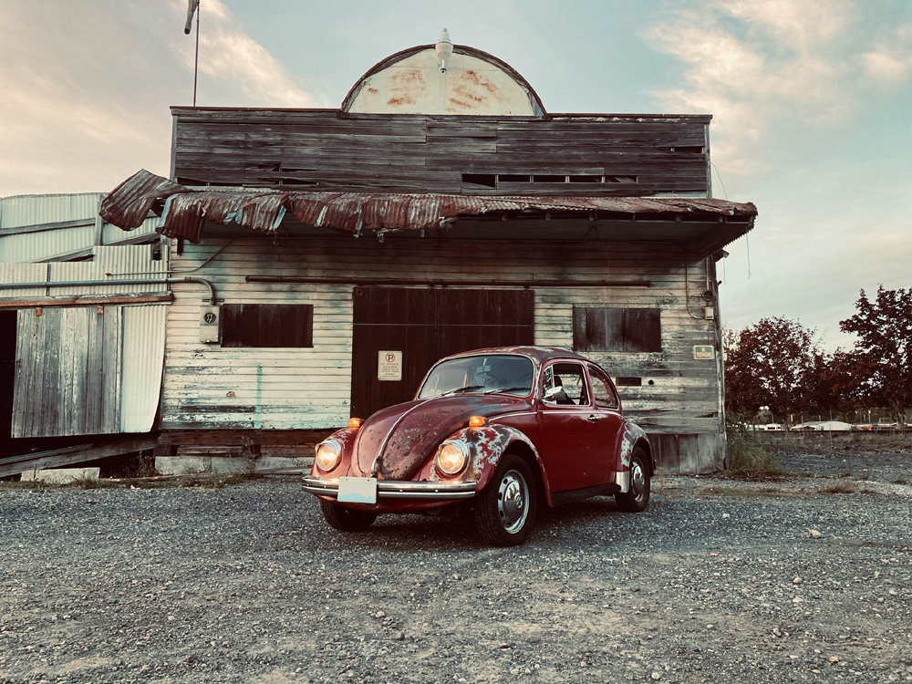 Red Beetle parked in front of a weathered wooden building with rustic backdrop
