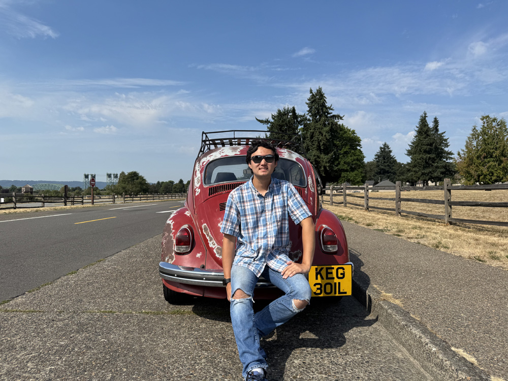 Logan sitting on rear bumper of red Beetle with roof rack on a sunny roadside
