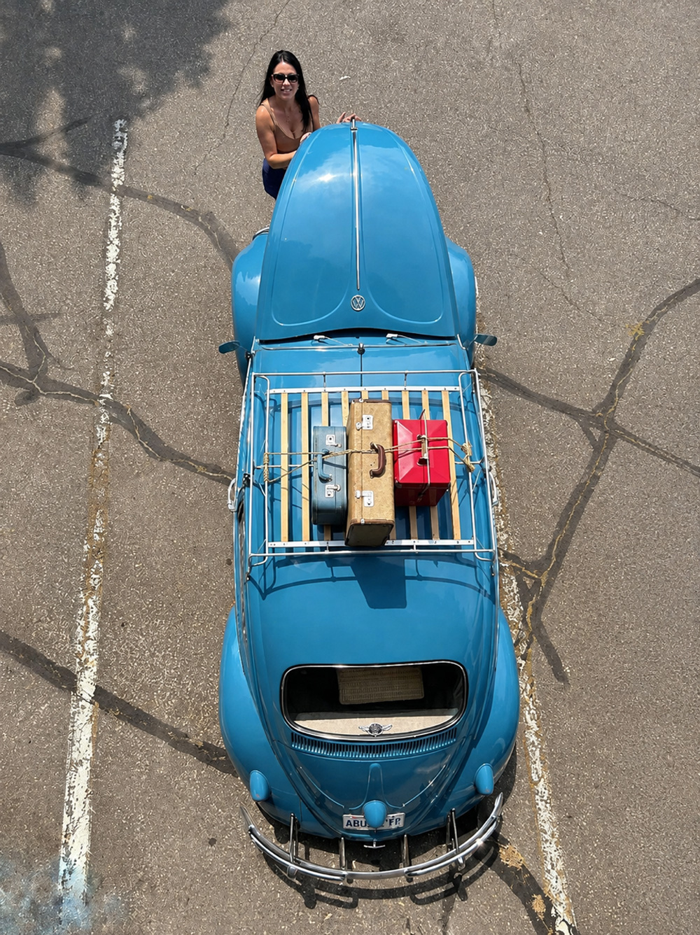 Overhead view of blue VW Beetle with roof-rack luggage and  the owner standing near the front