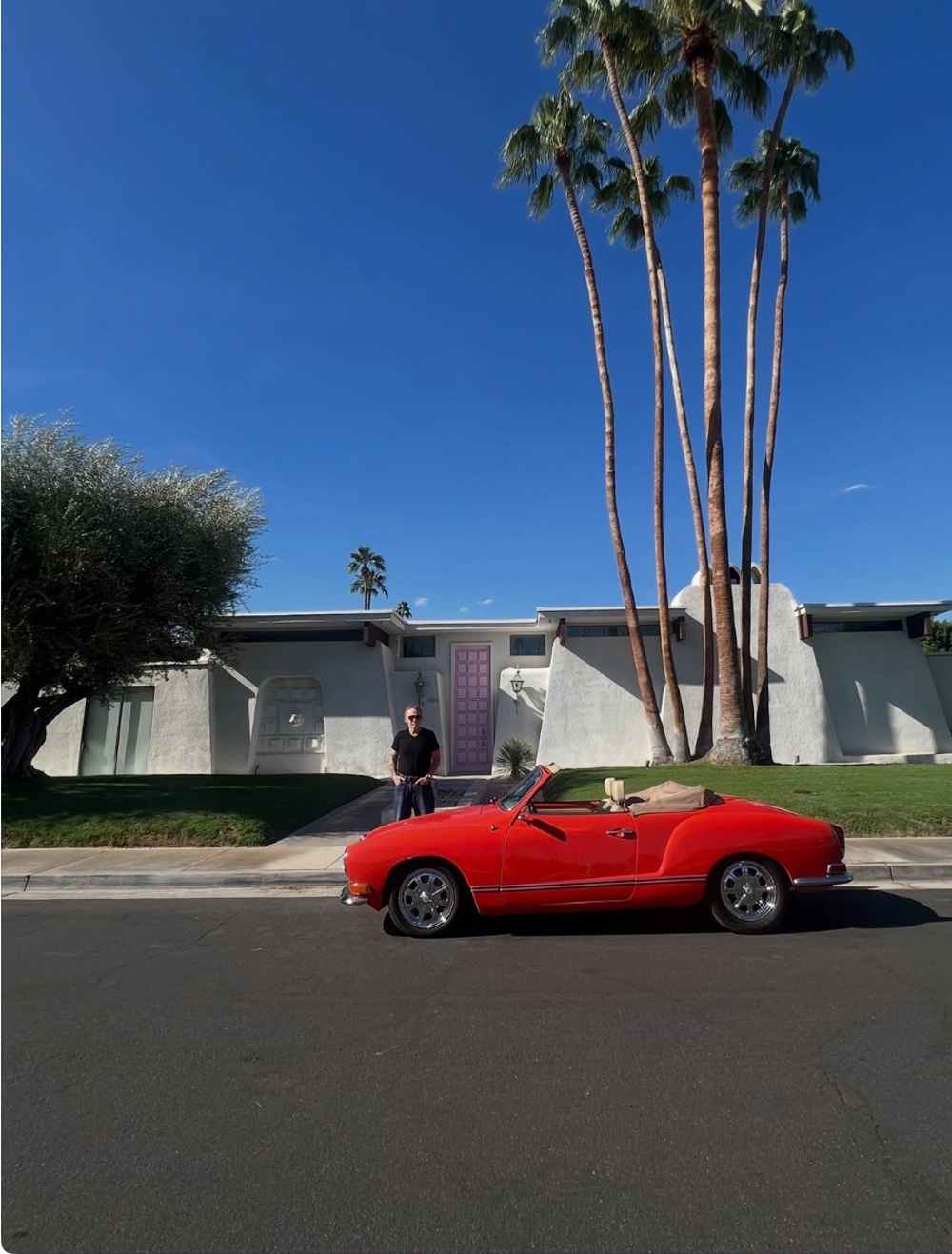 Red Karmann Ghia convertible parked in front of a mid century modern Palm Springs home with a pink front door