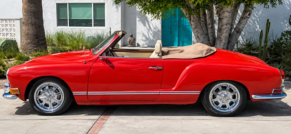 Red Karmann Ghia convertible parked in front of a white building with a turquoise door in Palm Springs