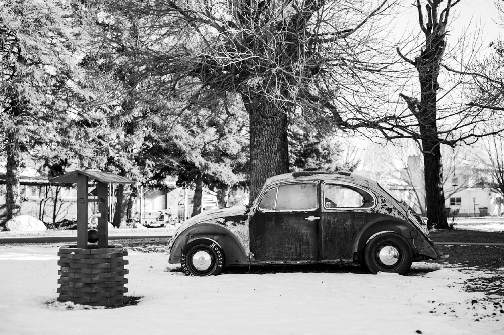 A vintage VW Beetle steadily climbing a snow-covered hill, its rear-mounted engine providing the necessary downforce for the tires to grip the slippery surface while modern cars struggle in the background.
