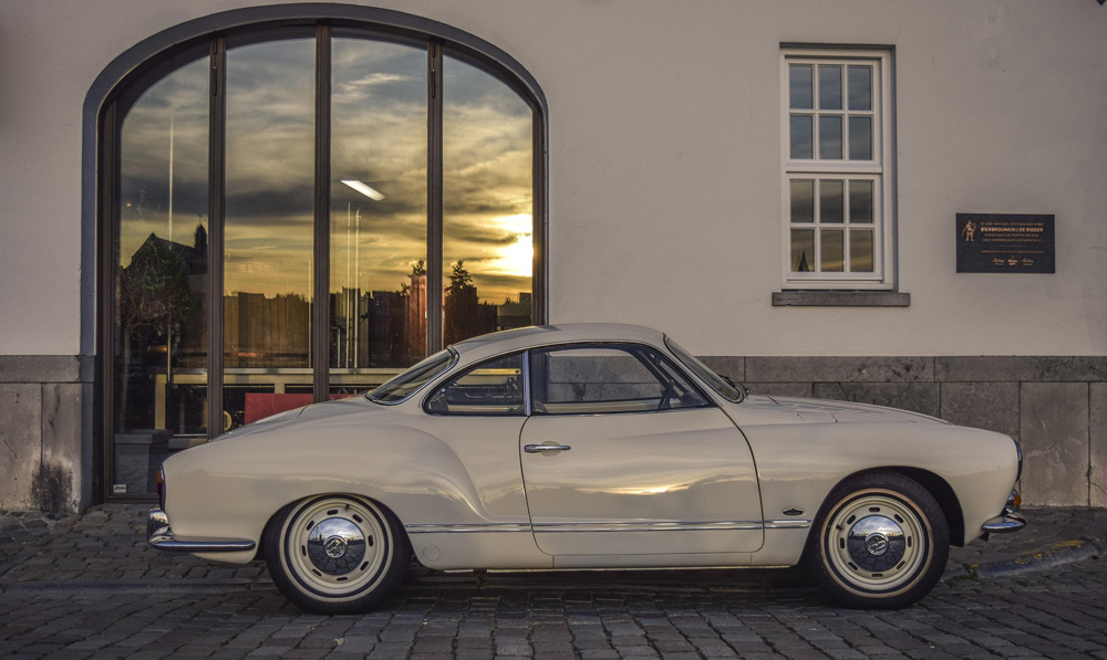 Cream colored Volkswagen Karmann Ghia on a cobblestone street, showing air cooled sports car design