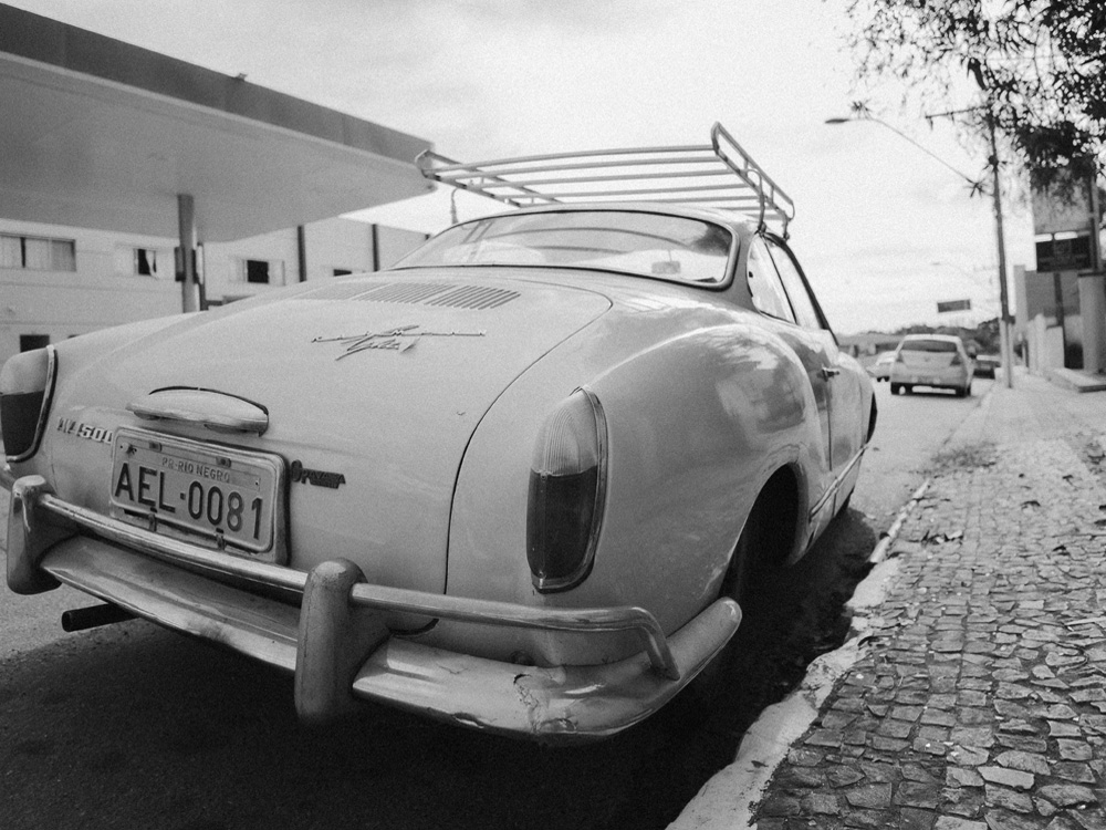 Black and white Karmann Ghia parked on cobblestone street with roof rack