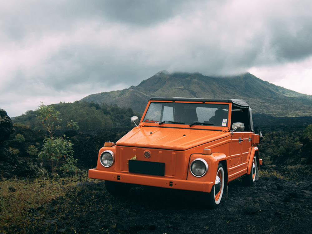 Orange Volkswagen Thing parked on volcanic landscape with mountain backdrop