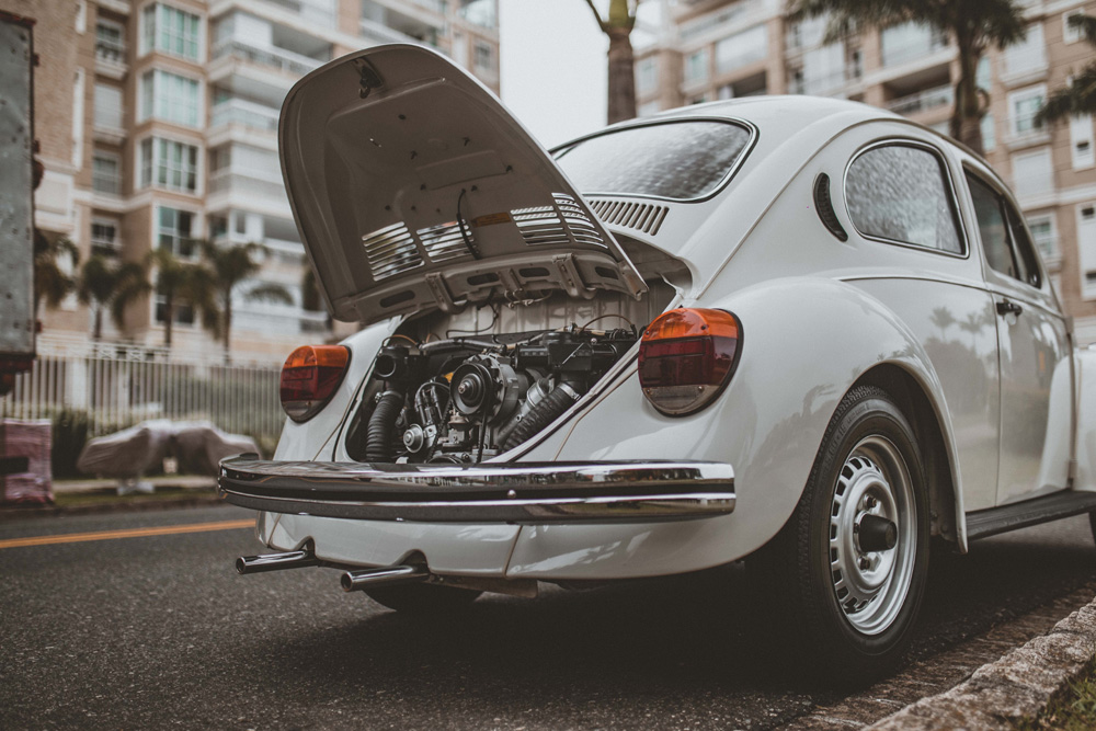 White Volkswagen Beetle parked with rear engine compartment open on city street