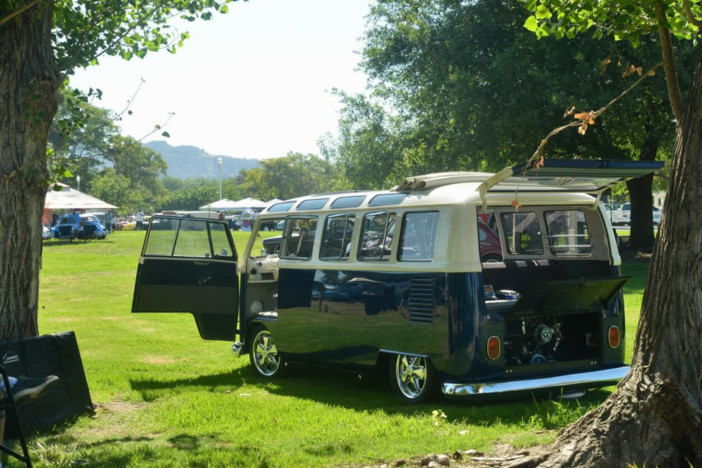 Two tone Volkswagen Bus with open engine and side door parked on the grass at the El Prado VW Show & Shine