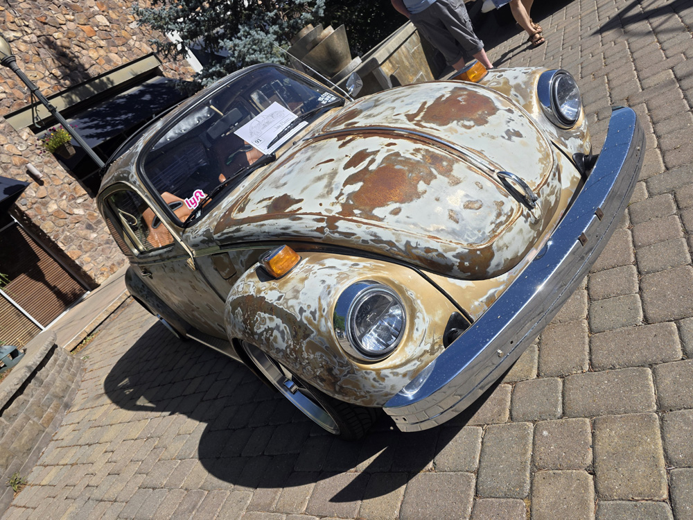 Weathered patina Volkswagen Beetle parked on cobblestone street at the show