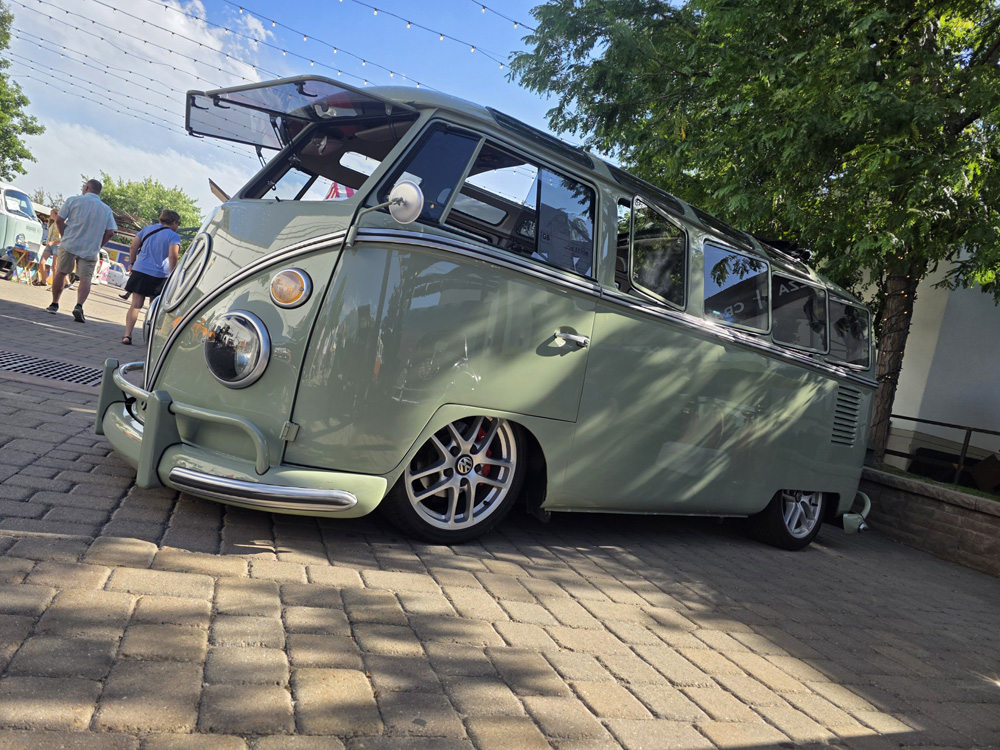 Light green lowered VW Bus with open windshield displayed under string lights