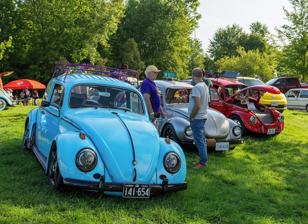 Bright blue Volkswagen Beetle in excellent condition at VW Legends 2026, with an Ontario plate and spectators interacting beside the car