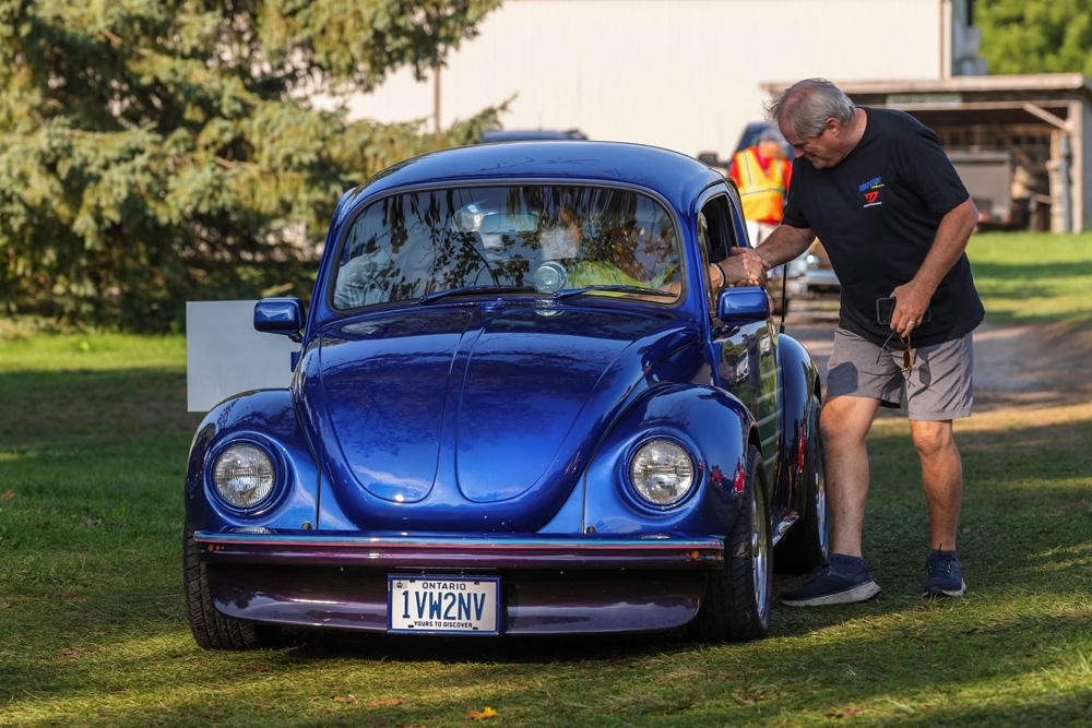 Bright blue Volkswagen Beetle in excellent condition at VW Legends 2026, with an Ontario plate and spectators interacting beside the car