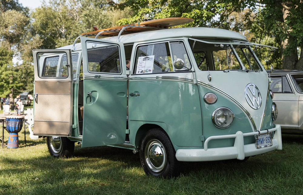 Mint green and white Volkswagen Bus with doors open and a surfboard on the roof at VW Legends 2026, displayed on the Plunkett Estate grounds