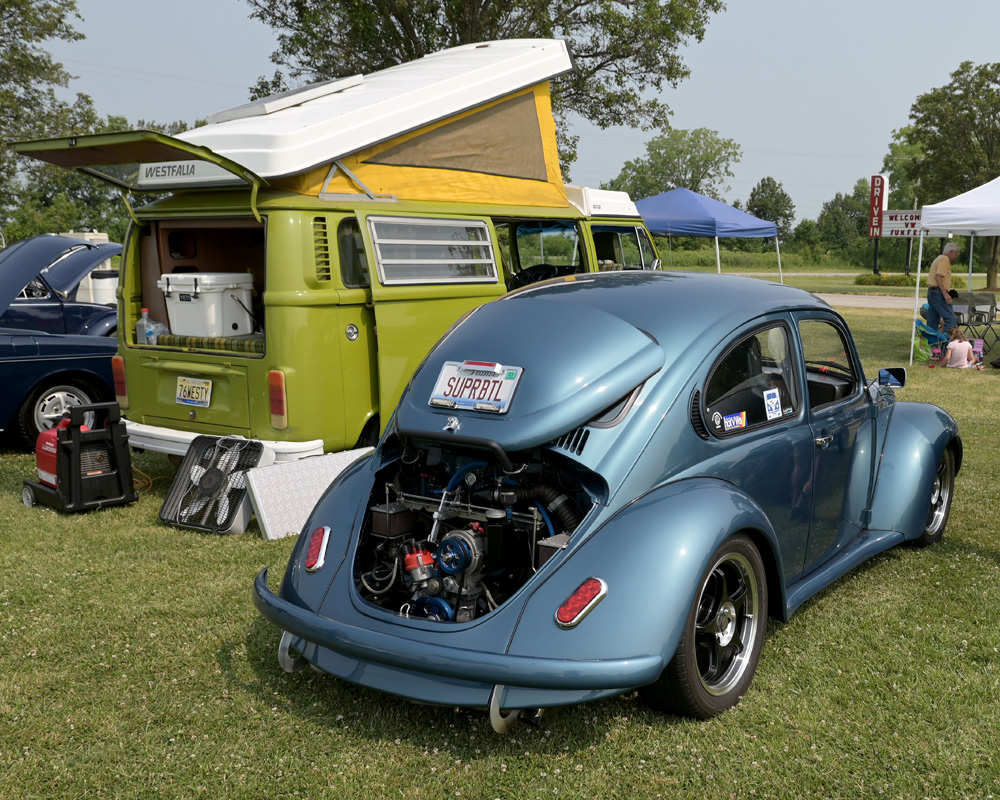 Classic Volkswagen Beetle and Westfalia camper on display at an outdoor Funfest event with attendees and vintage VWs in the background