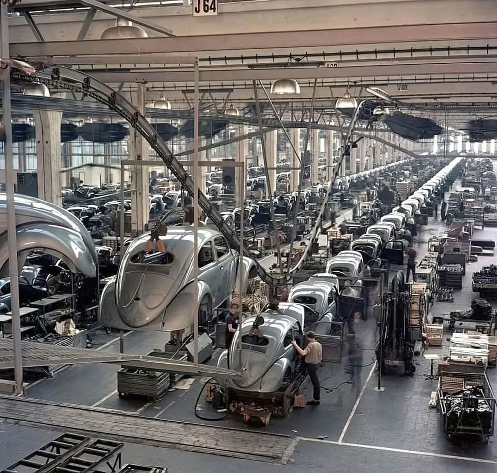 The iconic oval-window Beetle being assembled at Volkswagen's Wolfsburg factory, circa 1954. Note the overhead conveyors lowering the freshly painted car bodies onto the assembly lines below