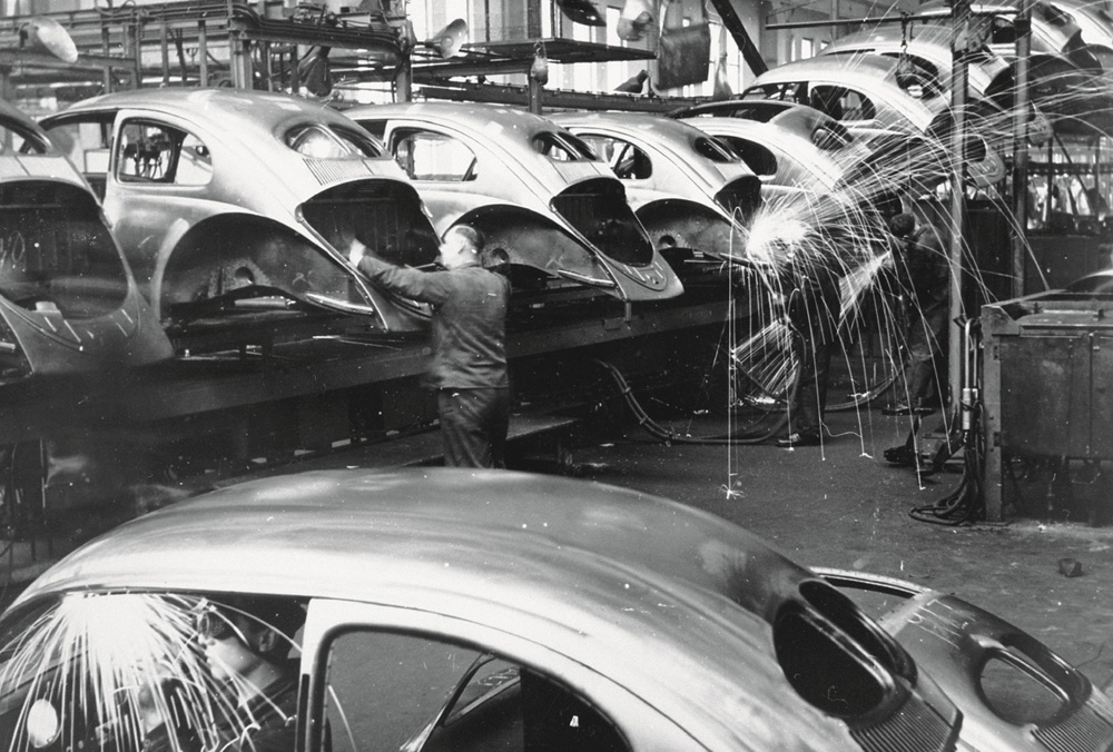 Sparks fly as Beetle bodyshells mounted transversely on a transfer line are welded by hand at the front and rear in 1952