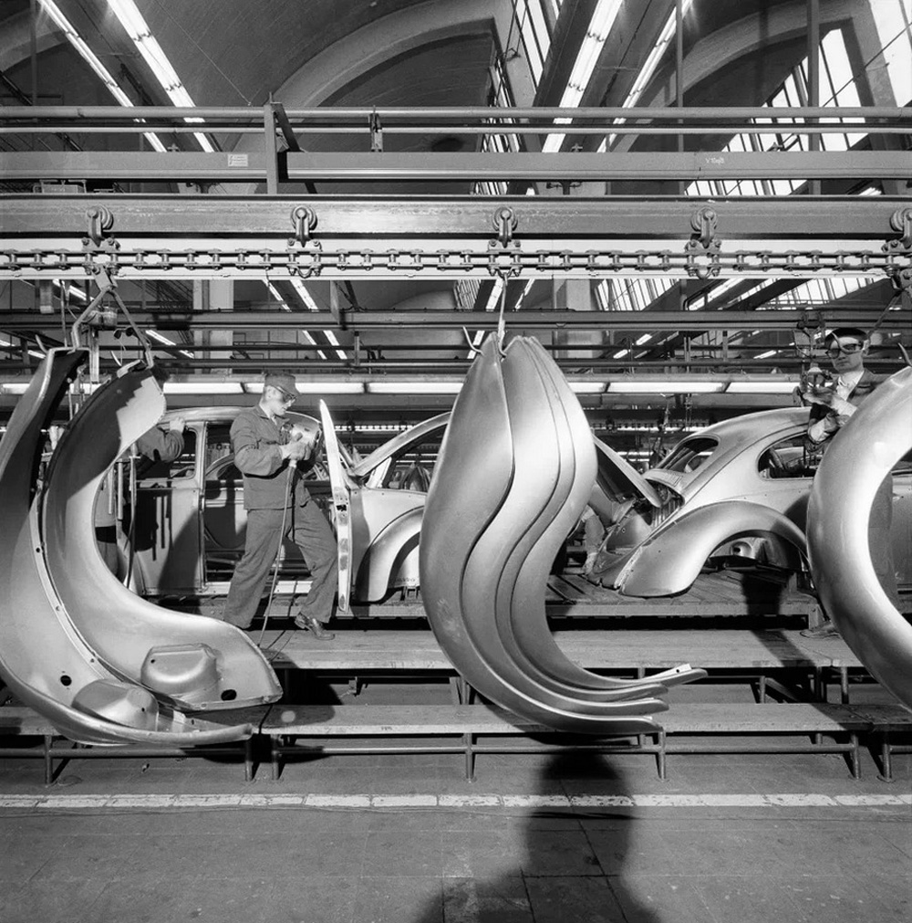 Front and rear fenders are passing the body assembly line in Wolfsburg, while a worker is doing the final touches to a right hand door.