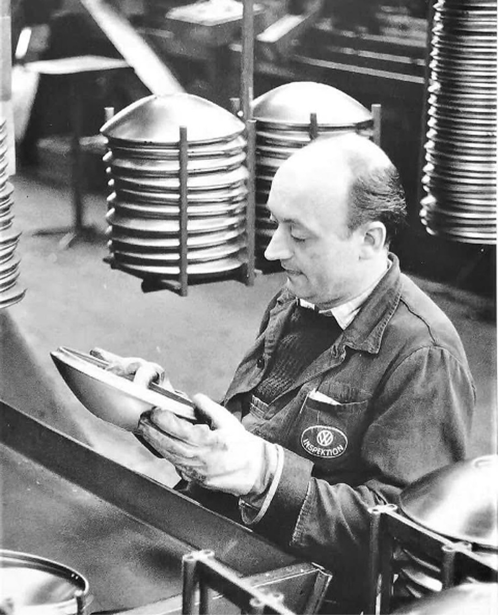 Volkswagen factory inspector checking a hubcap beside racks of parts during quality control