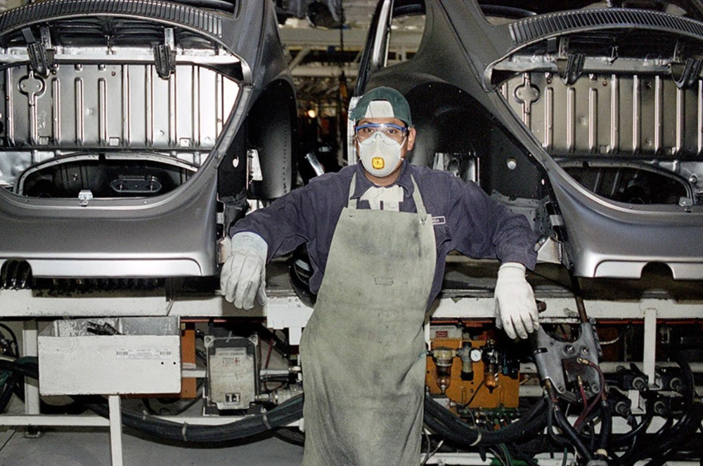 Volkswagen Puebla line worker posing beside partially assembled bodies on the production line in 2002