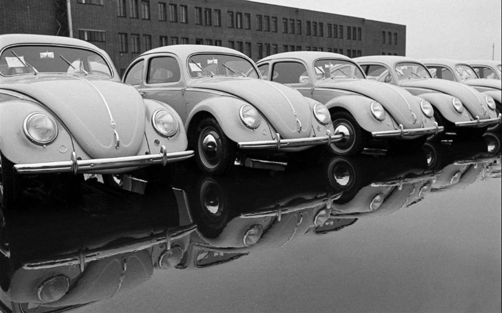 1951 Volkswagen export-model Beetles reflected in wet pavement outside the Wolfsburg administration building