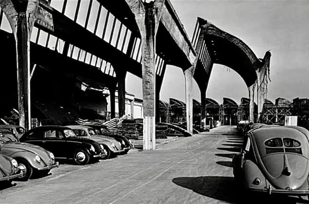 Postwar Wolfsburg factory with Beetles parked beside damaged concrete halls