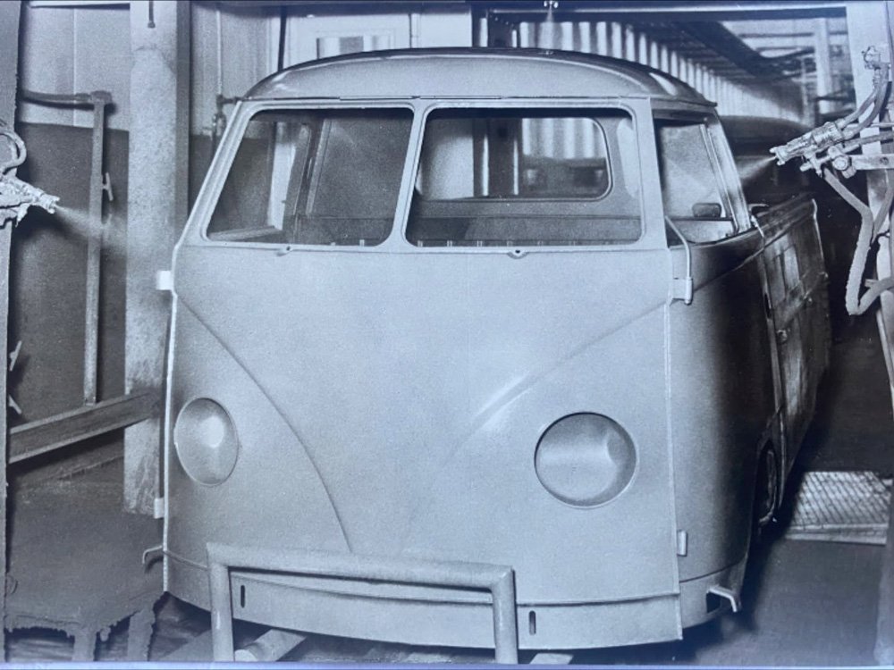 VW flatbed truck receiving automatic spraying as part of three-layer paint process.